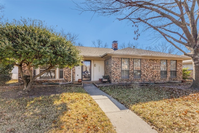 view of front facade featuring a front yard, brick siding, and a chimney