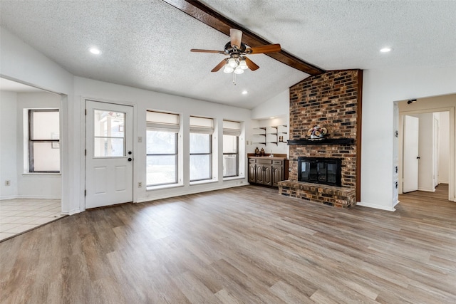 unfurnished living room featuring vaulted ceiling with beams, a fireplace, a textured ceiling, and light wood-type flooring