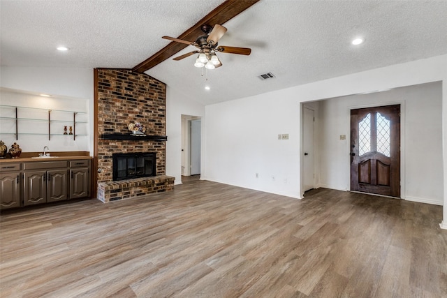 unfurnished living room with lofted ceiling with beams, a textured ceiling, and light wood-type flooring