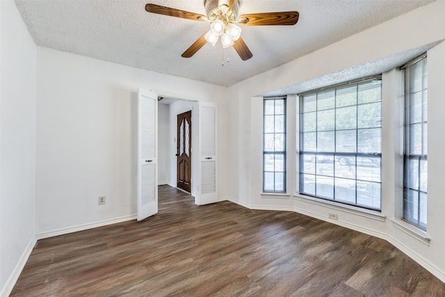 empty room featuring ceiling fan, dark wood-type flooring, a wealth of natural light, and a textured ceiling