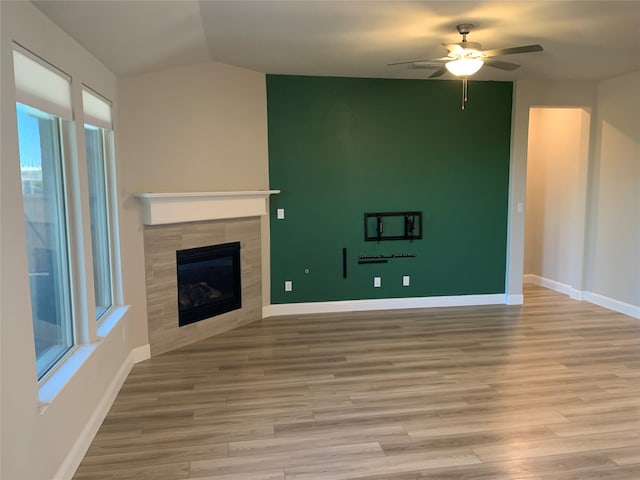 unfurnished living room with a tile fireplace, vaulted ceiling, ceiling fan, and light wood-type flooring