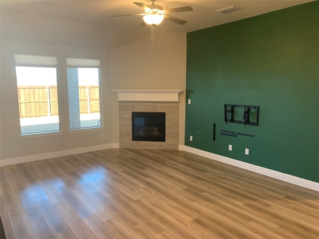 unfurnished living room featuring ceiling fan, lofted ceiling, a tile fireplace, and light hardwood / wood-style flooring