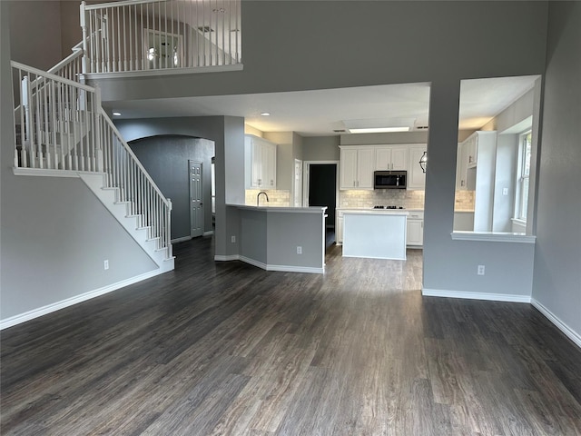 unfurnished living room featuring recessed lighting, a sink, baseboards, stairway, and dark wood-style floors