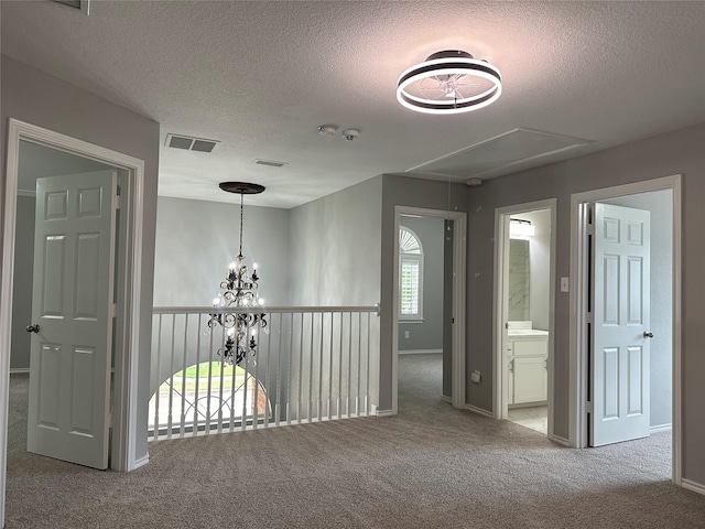 hallway featuring carpet, visible vents, a chandelier, and attic access