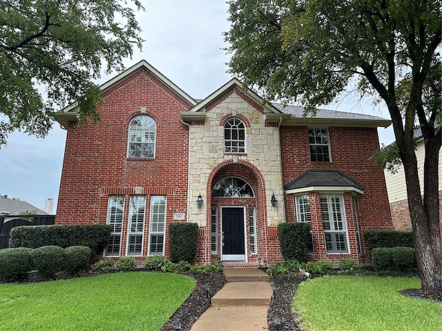 traditional-style house featuring a front yard, stone siding, and brick siding