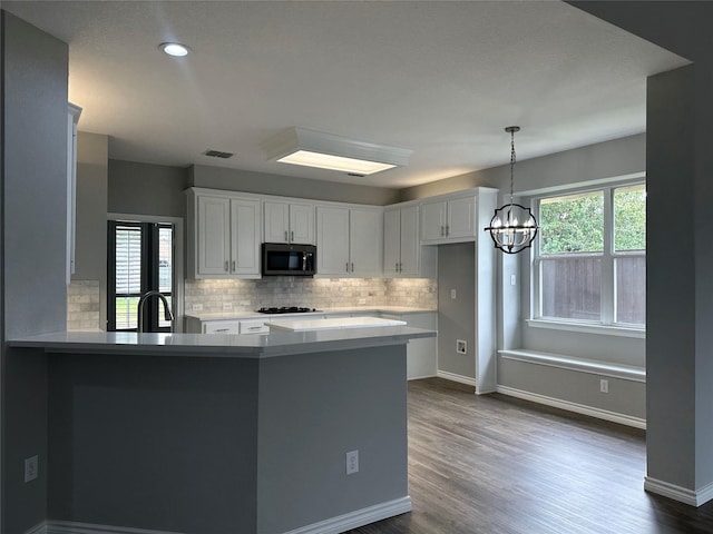 kitchen with a chandelier, a peninsula, dark wood-type flooring, white cabinetry, and light countertops