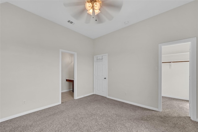 unfurnished bedroom featuring a walk in closet, light colored carpet, a closet, and ceiling fan