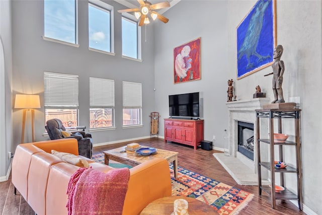 living room with ceiling fan, wood-type flooring, a high end fireplace, and a high ceiling