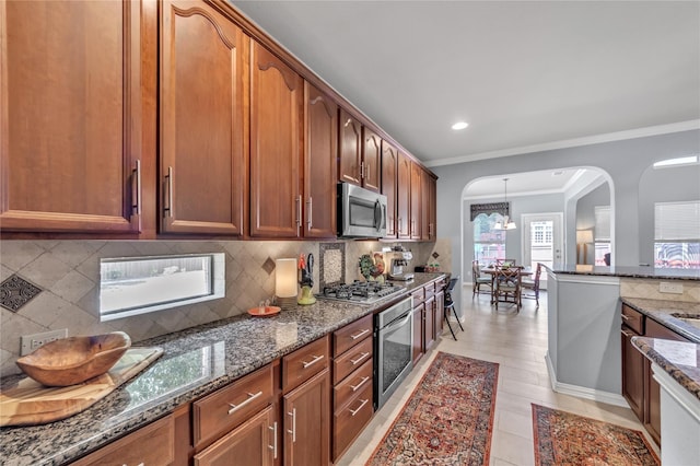 kitchen featuring pendant lighting, appliances with stainless steel finishes, backsplash, ornamental molding, and dark stone counters