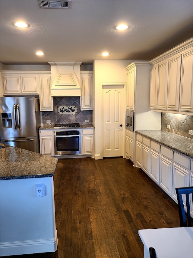 kitchen with custom exhaust hood, tasteful backsplash, dark stone countertops, dark hardwood / wood-style floors, and stainless steel appliances