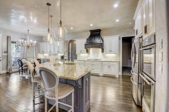 kitchen featuring pendant lighting, sink, white cabinets, custom range hood, and a center island with sink