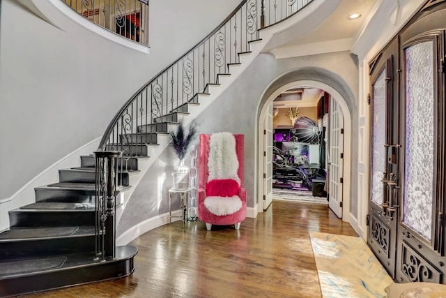 foyer with baseboards, arched walkways, a towering ceiling, wood finished floors, and french doors