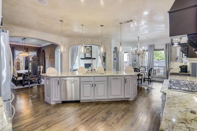 kitchen featuring hanging light fixtures, a kitchen island, light stone countertops, and appliances with stainless steel finishes