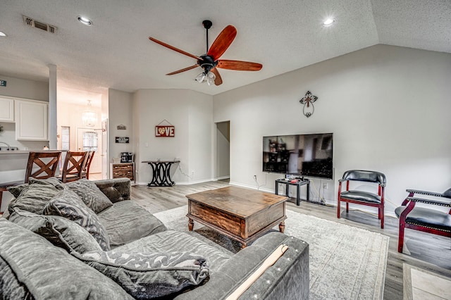 living room with ceiling fan, vaulted ceiling, a textured ceiling, and light wood-type flooring