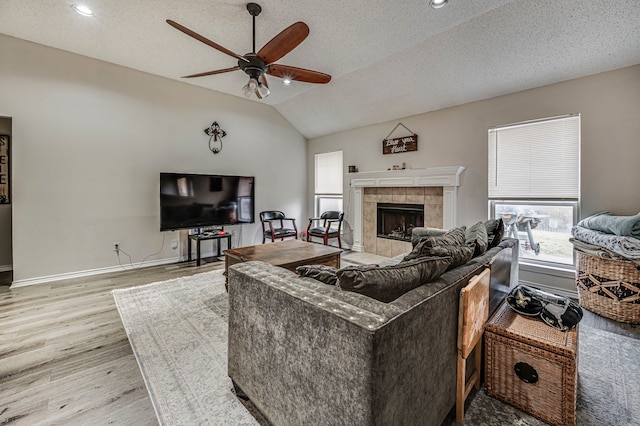 living room with lofted ceiling, ceiling fan, light hardwood / wood-style floors, a textured ceiling, and a tiled fireplace