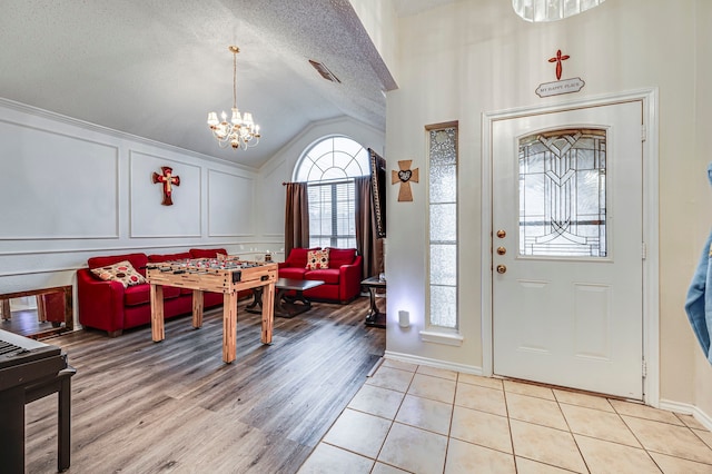 foyer featuring lofted ceiling, a notable chandelier, light hardwood / wood-style floors, and a textured ceiling