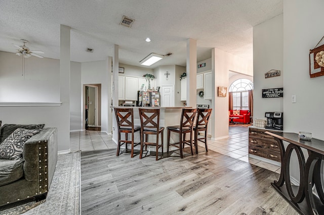 kitchen featuring a breakfast bar, white cabinetry, stainless steel fridge, light hardwood / wood-style floors, and a textured ceiling