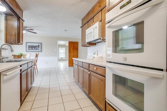 kitchen featuring sink, white appliances, light tile patterned floors, ceiling fan, and a textured ceiling