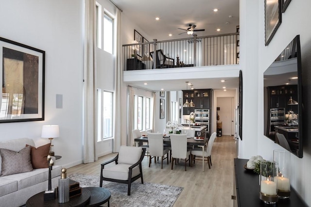 living room featuring a towering ceiling, ceiling fan, and light hardwood / wood-style flooring