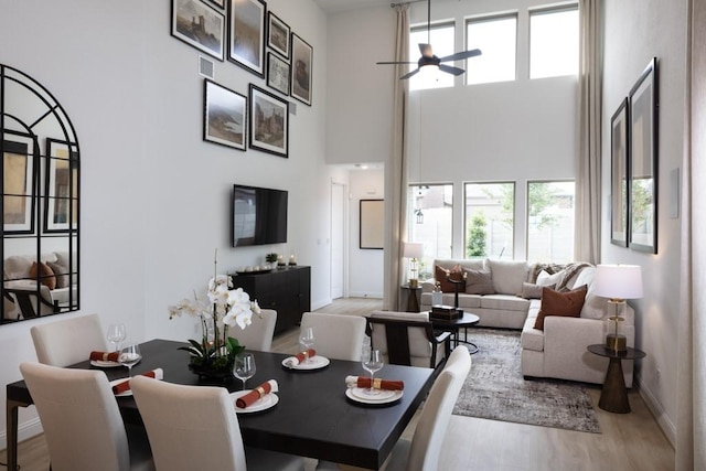 dining room featuring ceiling fan, a towering ceiling, and light hardwood / wood-style floors