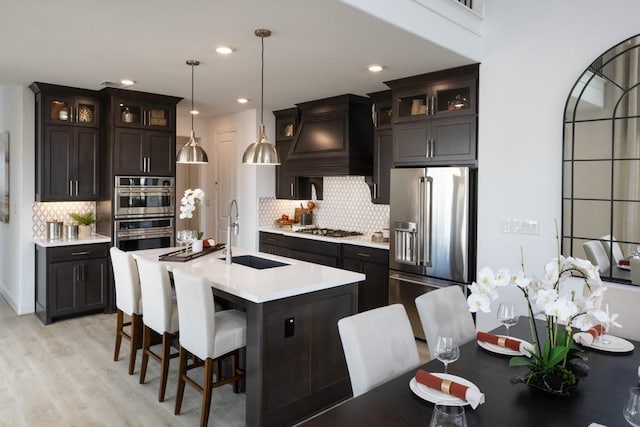 kitchen featuring sink, decorative light fixtures, an island with sink, stainless steel appliances, and light hardwood / wood-style floors