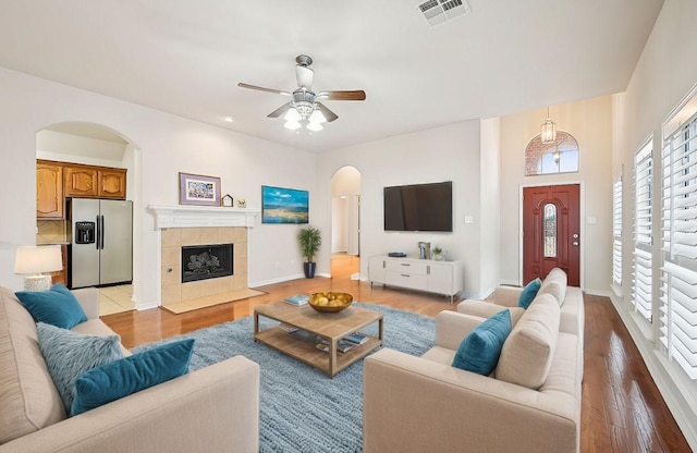 living room with light hardwood / wood-style floors, a tile fireplace, and ceiling fan