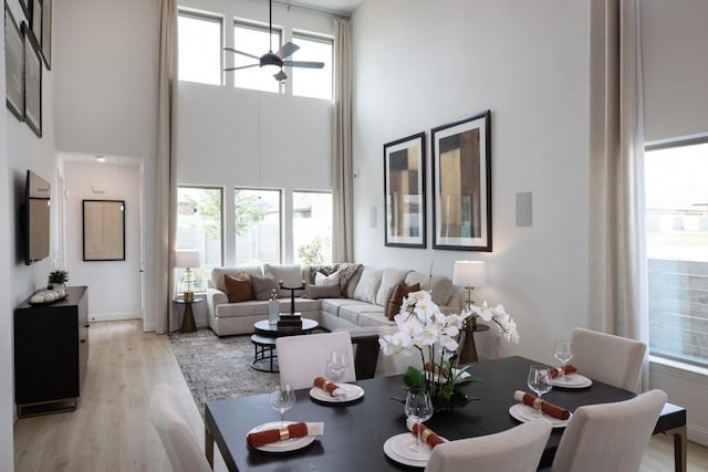 living room with ceiling fan, a towering ceiling, and light hardwood / wood-style floors