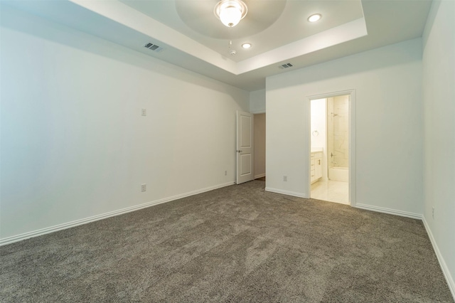 unfurnished bedroom with connected bathroom, a tray ceiling, and carpet flooring