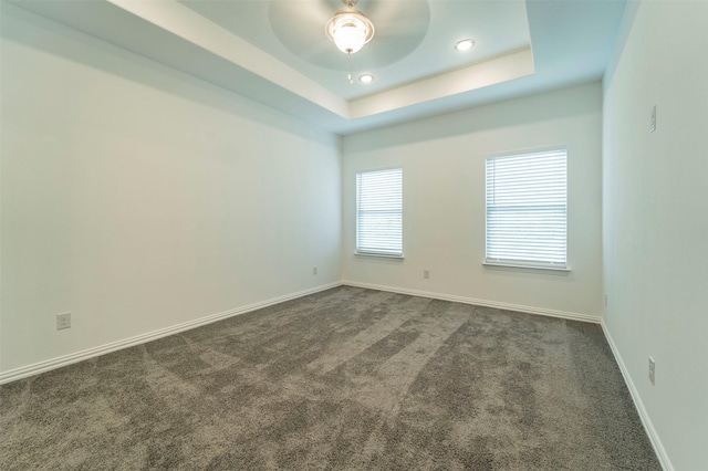 empty room featuring a raised ceiling and dark colored carpet