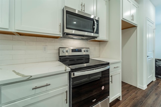 kitchen with dark wood-type flooring, appliances with stainless steel finishes, white cabinetry, tasteful backsplash, and light stone countertops