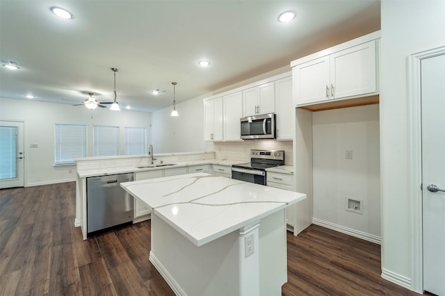 kitchen with sink, appliances with stainless steel finishes, hanging light fixtures, white cabinets, and a kitchen island