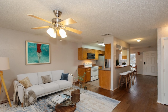 living area featuring visible vents, a ceiling fan, a textured ceiling, baseboards, and dark wood-style flooring