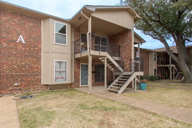 rear view of property with a yard, brick siding, and stairs