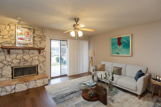 living area with hardwood / wood-style floors, a stone fireplace, a ceiling fan, and a textured ceiling