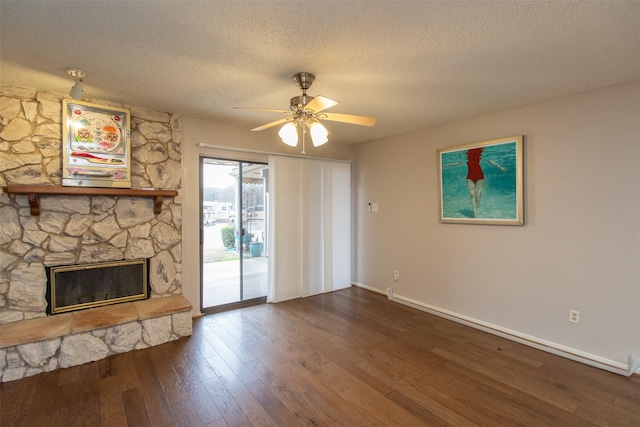 unfurnished living room with baseboards, ceiling fan, a stone fireplace, dark wood-type flooring, and a textured ceiling