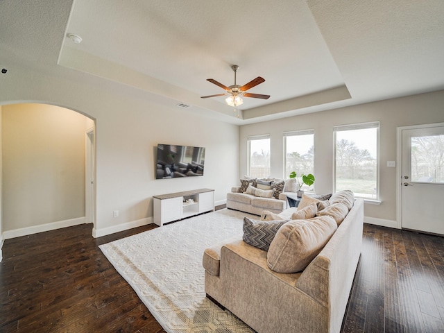 living room with dark hardwood / wood-style floors, a raised ceiling, and ceiling fan