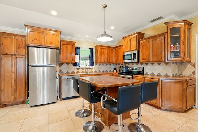 kitchen with stainless steel appliances, brown cabinets, ornamental molding, glass insert cabinets, and light tile patterned flooring