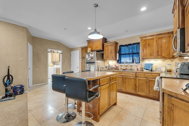 kitchen with vaulted ceiling, a kitchen island, appliances with stainless steel finishes, hanging light fixtures, and crown molding