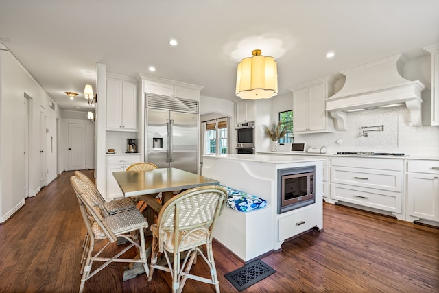 kitchen featuring built in appliances, tasteful backsplash, custom range hood, and white cabinets