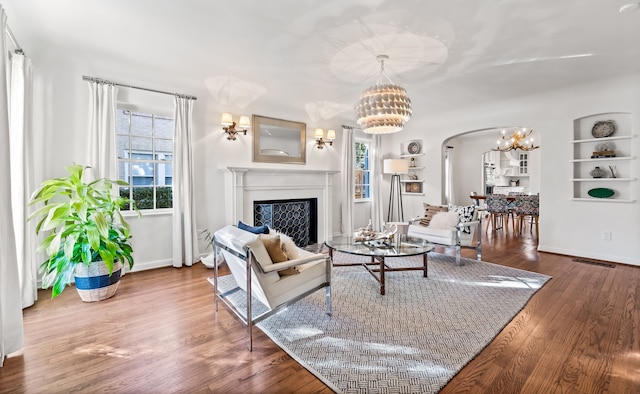 living room with built in shelves, a healthy amount of sunlight, a chandelier, and hardwood / wood-style floors