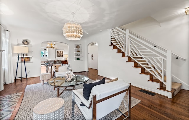 living room with dark wood-type flooring, an inviting chandelier, and built in shelves