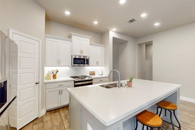 kitchen featuring stainless steel appliances, a center island with sink, and white cabinets