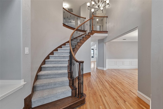 staircase with hardwood / wood-style flooring, an inviting chandelier, and a high ceiling