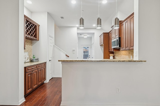 kitchen featuring light stone counters, pendant lighting, stainless steel microwave, and brown cabinetry