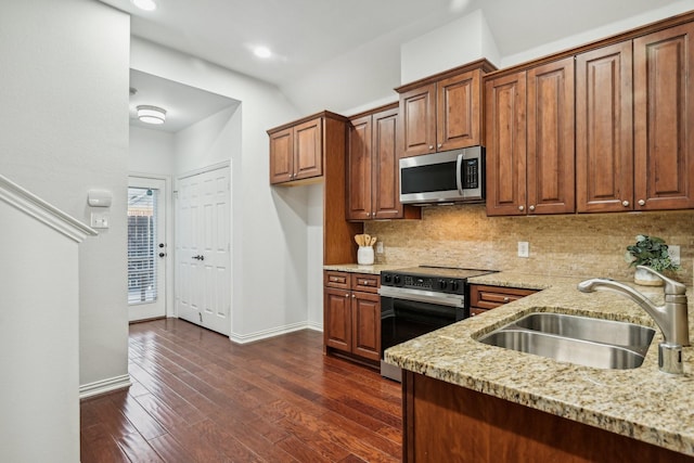 kitchen featuring light stone counters, stainless steel appliances, decorative backsplash, dark wood-type flooring, and a sink