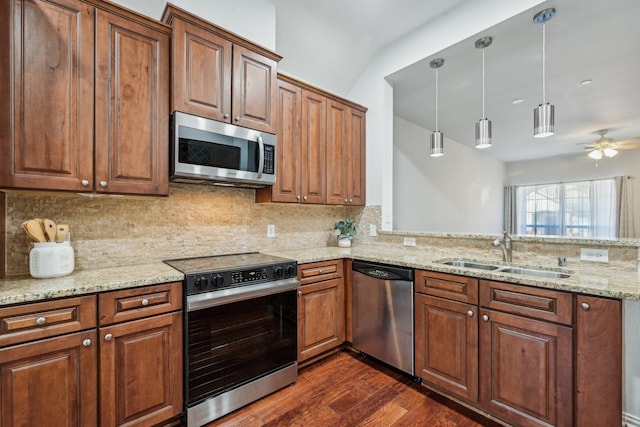 kitchen featuring light stone counters, a sink, appliances with stainless steel finishes, brown cabinets, and decorative light fixtures