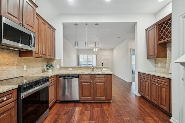 kitchen featuring appliances with stainless steel finishes, light stone counters, decorative light fixtures, a peninsula, and a sink