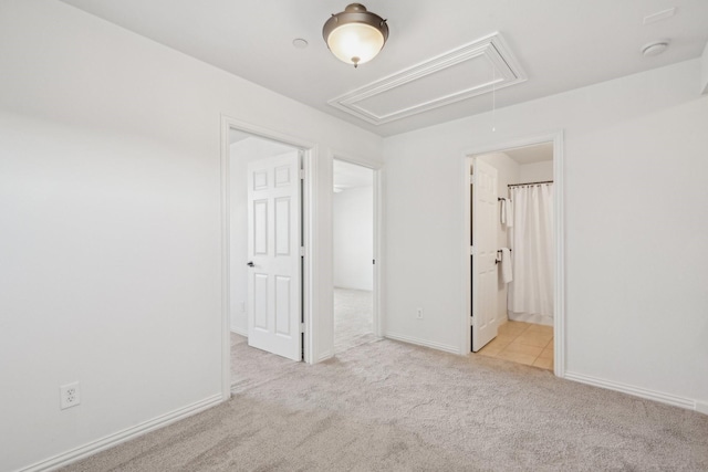 unfurnished bedroom with a spacious closet, attic access, light carpet, ensuite bath, and baseboards