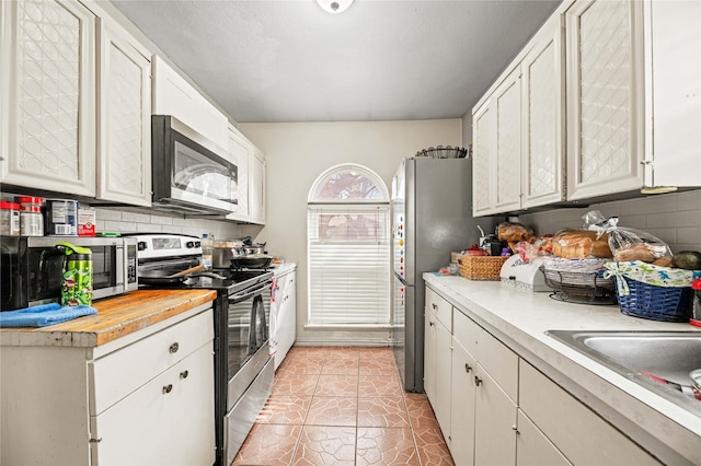 kitchen featuring sink, white cabinetry, backsplash, stainless steel appliances, and light tile patterned flooring