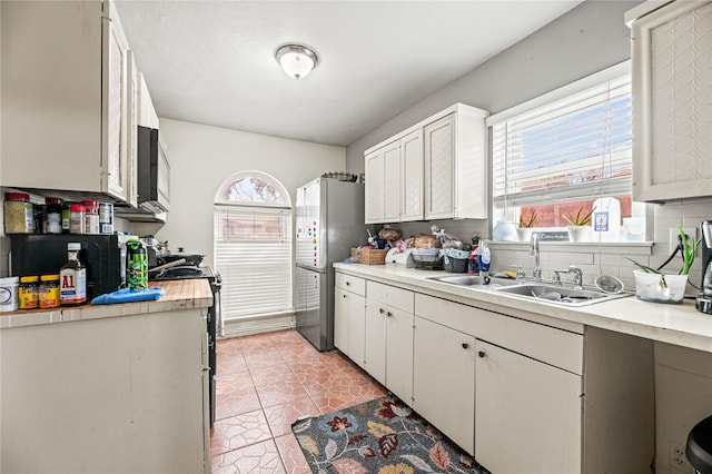 kitchen with sink, plenty of natural light, stainless steel refrigerator, and white cabinets